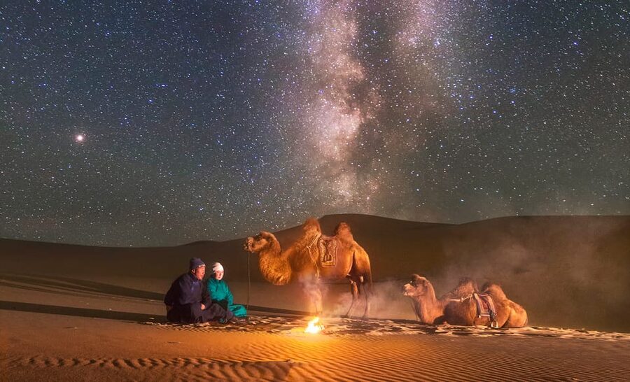Camels resting beside a fire under the Milky Way in central Mongolia